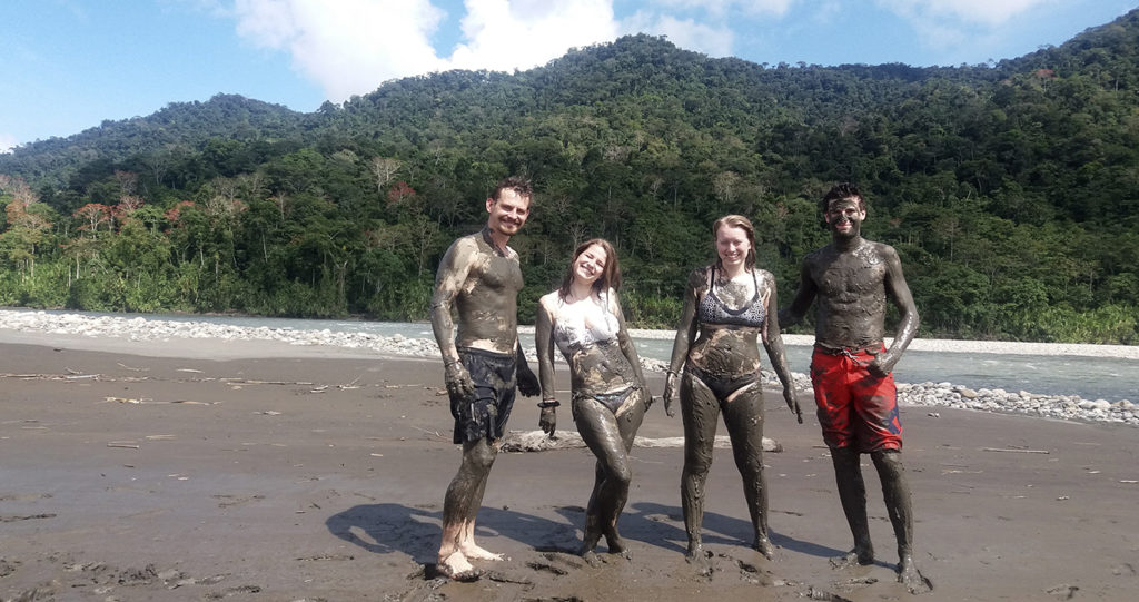 Viajeros cubiertos de arcilla en una playa del río durante la terapia de arcilla