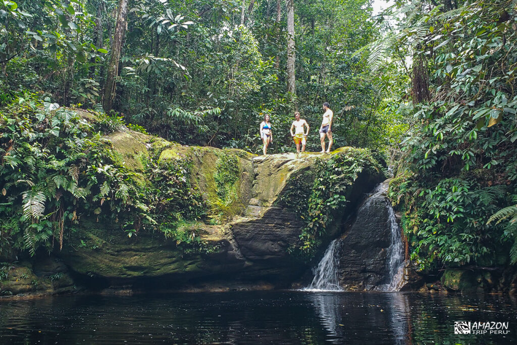 Travelers on a rock above a waterfall pool in the forest